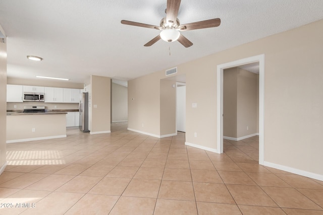 unfurnished living room with visible vents, a textured ceiling, light tile patterned floors, baseboards, and ceiling fan