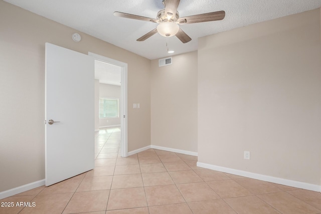 spare room featuring light tile patterned floors, a ceiling fan, baseboards, visible vents, and a textured ceiling