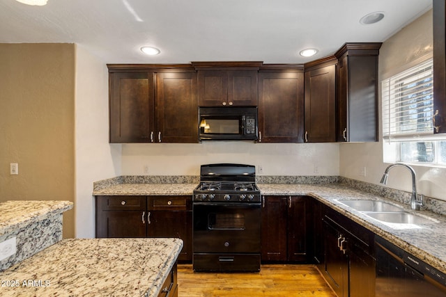 kitchen featuring sink, light stone counters, dark brown cabinets, light wood-type flooring, and black appliances