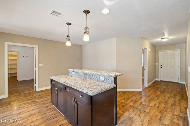 kitchen featuring dark brown cabinetry, light stone counters, a center island, hanging light fixtures, and dark hardwood / wood-style floors