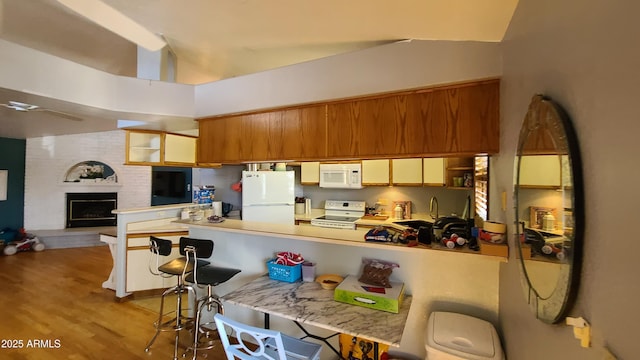 kitchen featuring a breakfast bar, a fireplace, kitchen peninsula, white appliances, and light hardwood / wood-style flooring