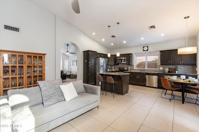 tiled living room featuring ceiling fan, high vaulted ceiling, and sink