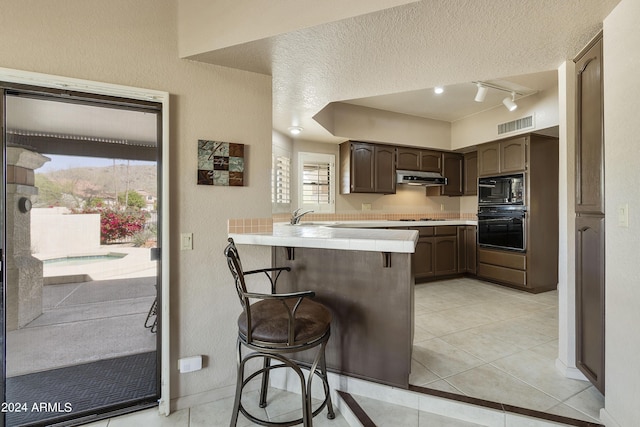 kitchen featuring a kitchen bar, kitchen peninsula, a textured ceiling, sink, and black appliances