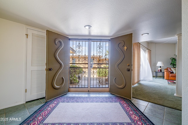 tiled entryway with carpet floors, baseboards, and a textured ceiling