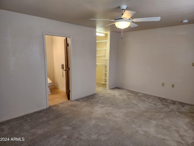 unfurnished bedroom featuring a walk in closet, ceiling fan, ensuite bath, and light carpet