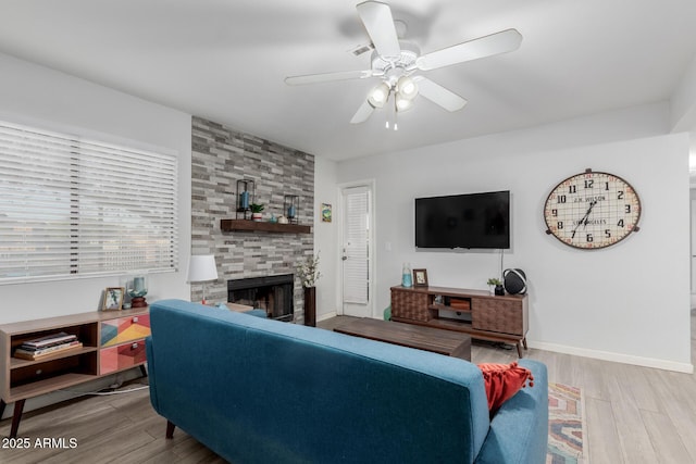 living room featuring ceiling fan, a healthy amount of sunlight, a stone fireplace, and light hardwood / wood-style flooring