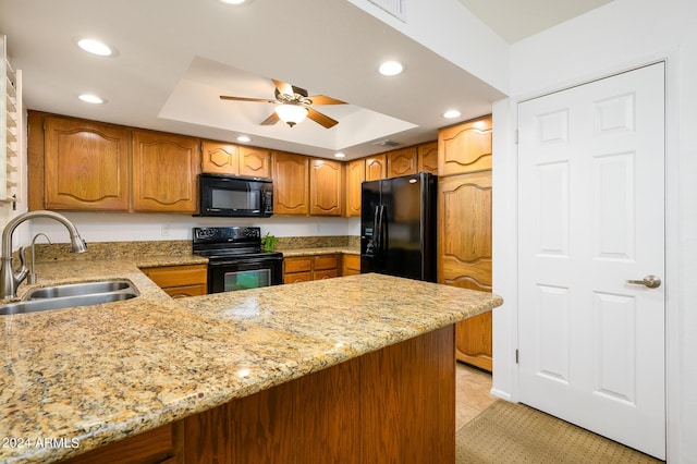 kitchen with sink, light stone counters, kitchen peninsula, a tray ceiling, and black appliances