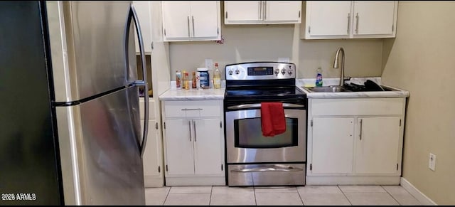 kitchen with a sink, appliances with stainless steel finishes, white cabinets, light tile patterned floors, and baseboards