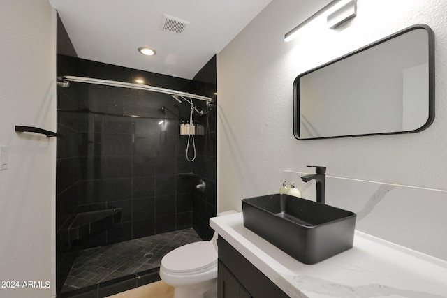 bathroom with a tile shower, vanity, and toilet