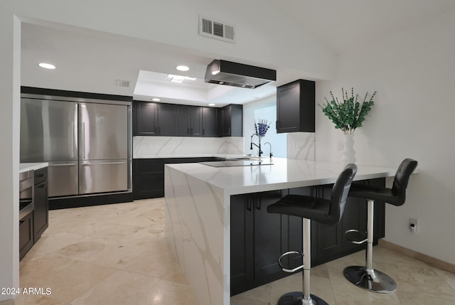 kitchen featuring a breakfast bar, lofted ceiling, kitchen peninsula, stainless steel refrigerator, and backsplash