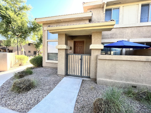 property entrance with a gate, stucco siding, and fence