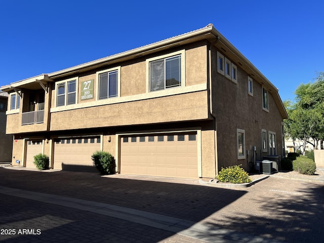 townhome / multi-family property featuring stucco siding, central AC, decorative driveway, and a garage