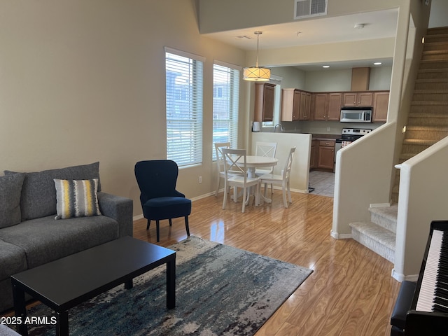 living room featuring stairway, light wood-style floors, visible vents, and baseboards