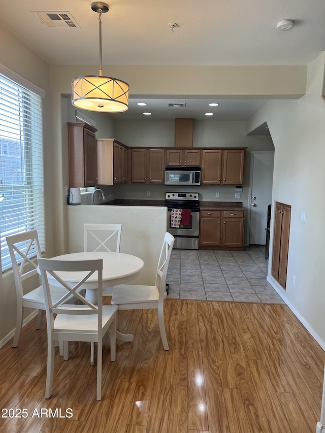 kitchen with stainless steel appliances, dark countertops, visible vents, and light wood finished floors