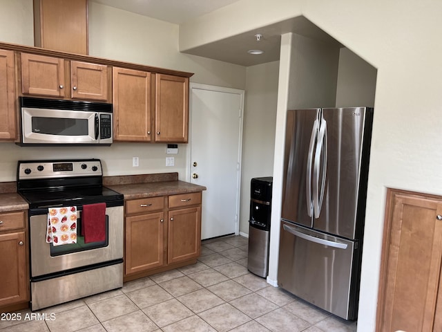 kitchen featuring light tile patterned floors, stainless steel appliances, brown cabinets, and dark countertops