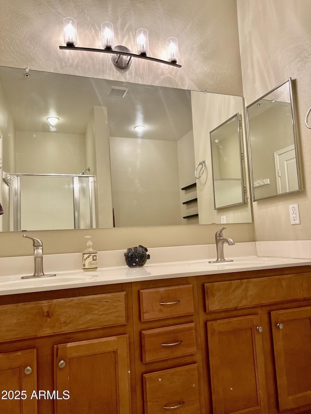 bathroom featuring double vanity, an enclosed shower, visible vents, and a sink