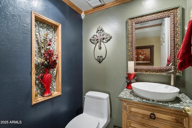 half bath with a textured wall, vanity, toilet, visible vents, and ornamental molding