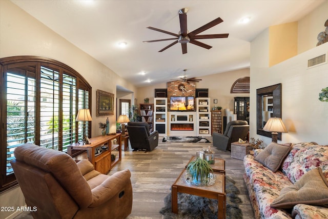 living area with a ceiling fan, visible vents, a fireplace, wood finished floors, and lofted ceiling