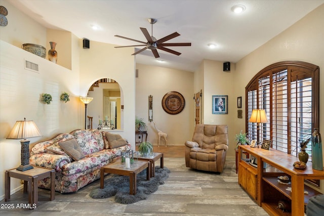 living area featuring ceiling fan, arched walkways, wood finished floors, vaulted ceiling, and visible vents