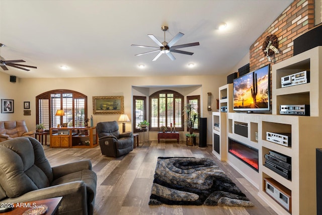 living room featuring a fireplace, a ceiling fan, and wood finished floors