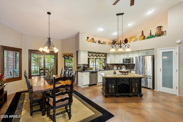 dining space with baseboards, ceiling fan with notable chandelier, high vaulted ceiling, and finished concrete floors