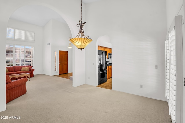 living area featuring arched walkways, a high ceiling, and light colored carpet