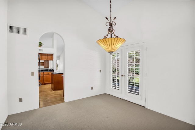 unfurnished dining area featuring light carpet, french doors, high vaulted ceiling, and arched walkways