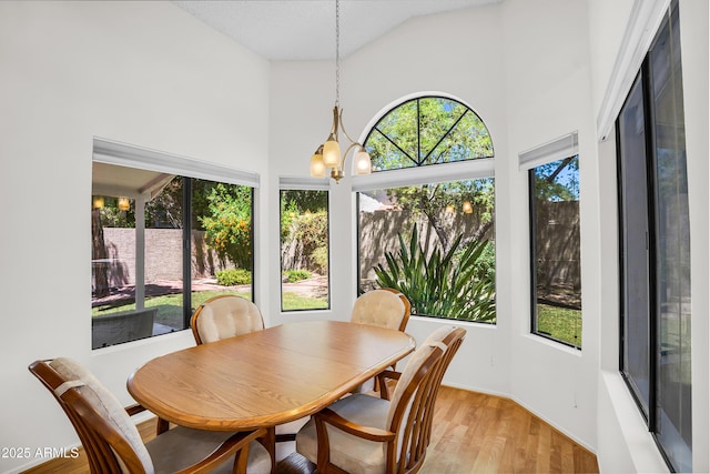 sunroom featuring high vaulted ceiling, wood finished floors, a chandelier, and baseboards
