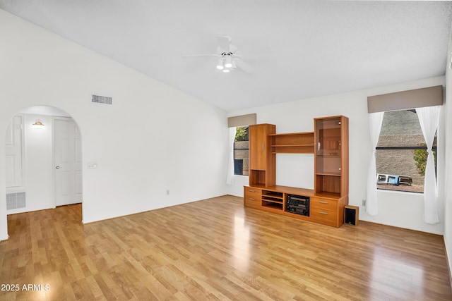 unfurnished living room with light wood-type flooring, ceiling fan, lofted ceiling, and arched walkways