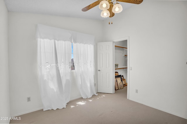 carpeted bedroom with vaulted ceiling, baseboards, a walk in closet, and ceiling fan