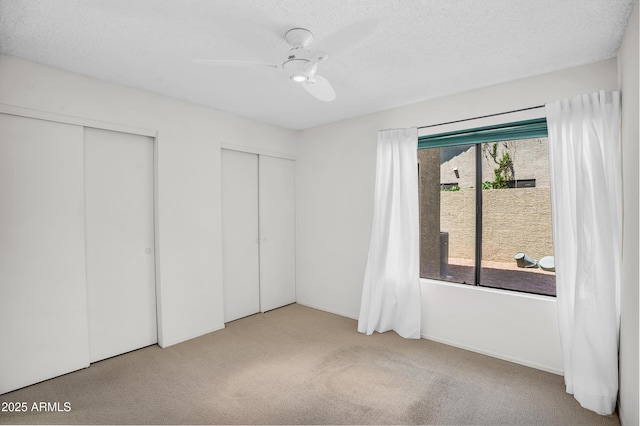 unfurnished bedroom featuring carpet floors, two closets, and ceiling fan