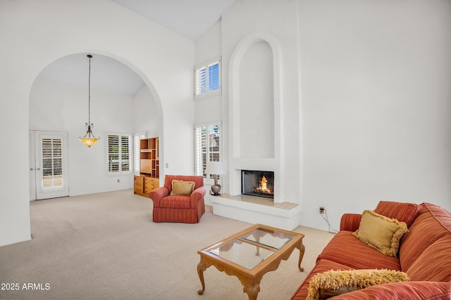 carpeted living area with high vaulted ceiling, arched walkways, and a fireplace