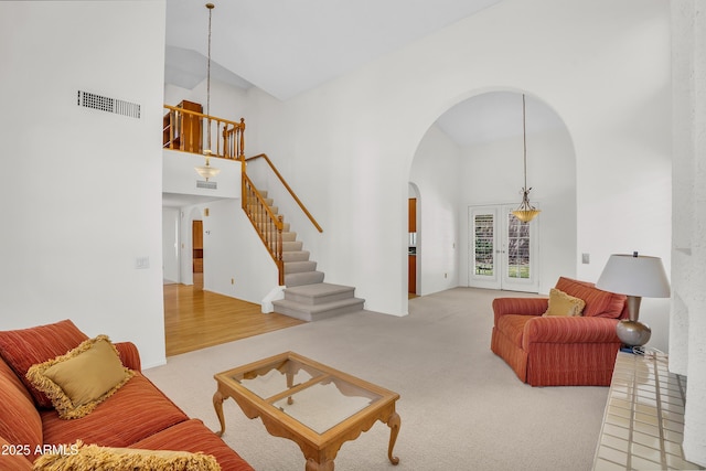 living area with high vaulted ceiling, arched walkways, light colored carpet, and stairway