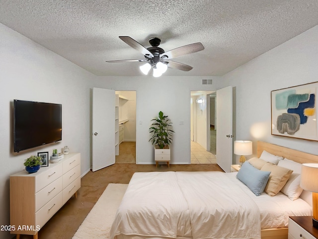 bedroom with a walk in closet, light colored carpet, visible vents, ceiling fan, and a textured ceiling