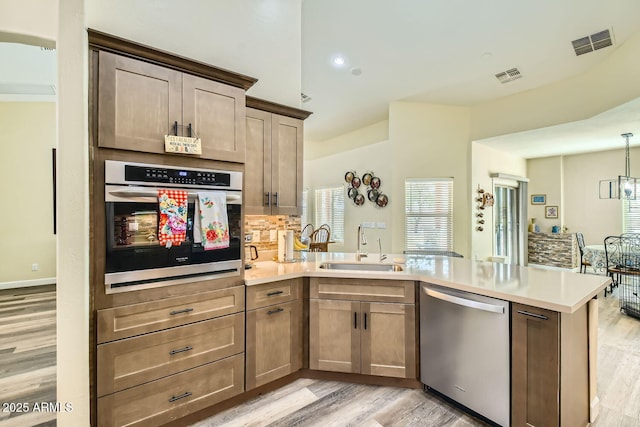 kitchen with appliances with stainless steel finishes, sink, light hardwood / wood-style flooring, and kitchen peninsula