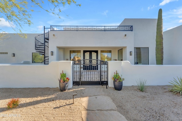 view of front of home with stucco siding, a gate, a fenced front yard, a balcony, and stairs