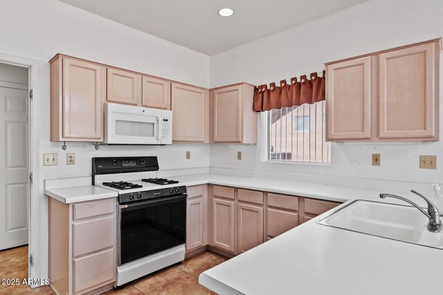kitchen with light brown cabinetry, a sink, light countertops, white microwave, and gas range oven