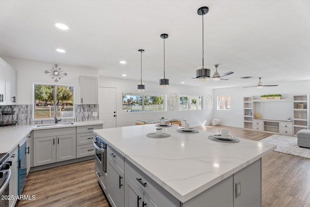 kitchen featuring wood finished floors, a sink, open floor plan, backsplash, and a center island