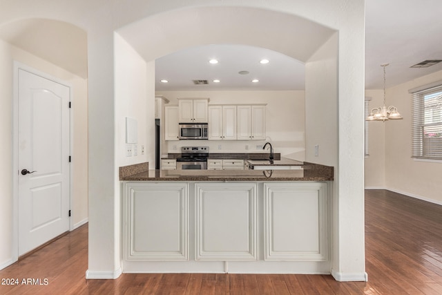 kitchen with appliances with stainless steel finishes, dark stone counters, pendant lighting, and hardwood / wood-style floors