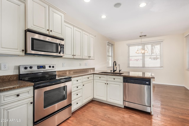 kitchen with kitchen peninsula, white cabinets, appliances with stainless steel finishes, light hardwood / wood-style flooring, and sink