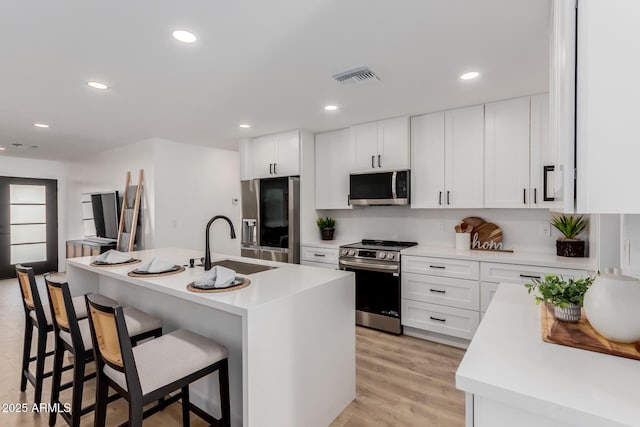 kitchen with white cabinetry, appliances with stainless steel finishes, a breakfast bar, and a center island with sink