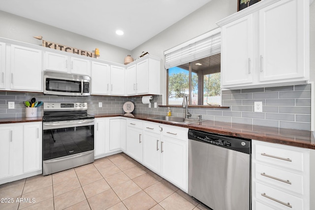 kitchen with light tile patterned floors, decorative backsplash, dark countertops, stainless steel appliances, and a sink