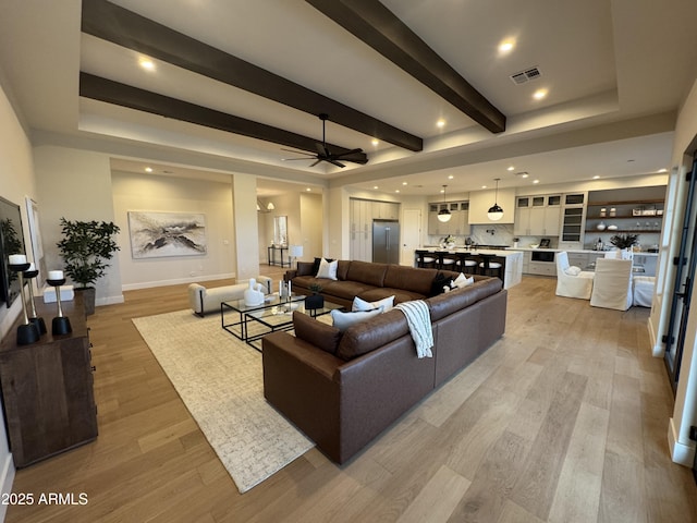 living room with visible vents, beam ceiling, baseboards, a ceiling fan, and light wood-style flooring