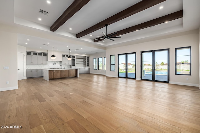 unfurnished living room featuring french doors, beam ceiling, light hardwood / wood-style flooring, sink, and ceiling fan