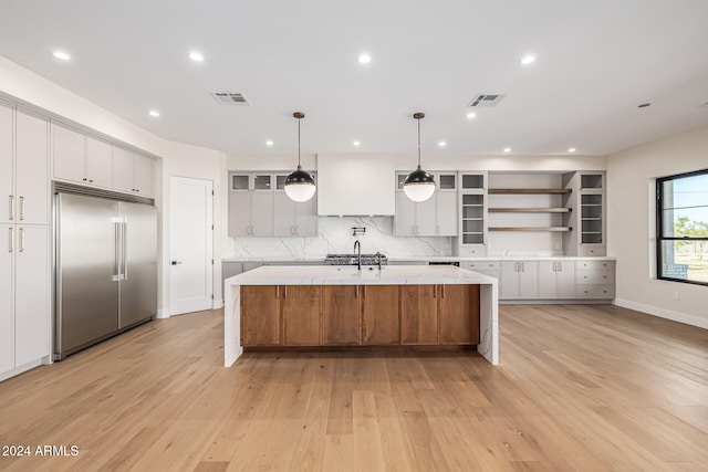 kitchen with a spacious island, white cabinetry, decorative light fixtures, built in refrigerator, and light hardwood / wood-style flooring