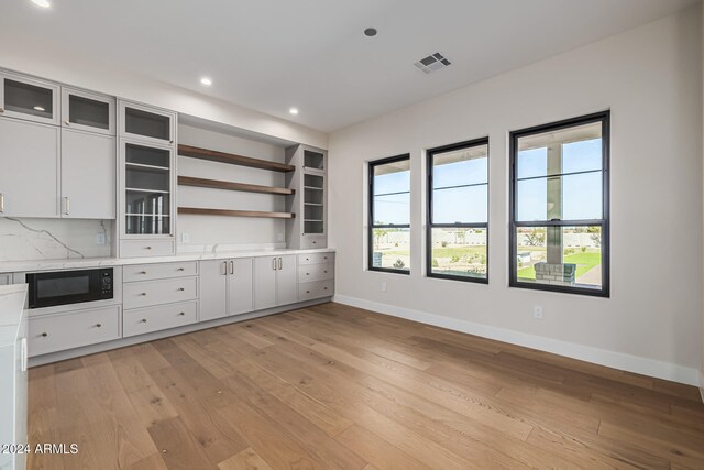 kitchen with light hardwood / wood-style floors, black microwave, white cabinets, and tasteful backsplash