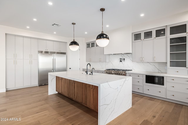 kitchen featuring light stone countertops, a kitchen island with sink, built in appliances, and white cabinetry