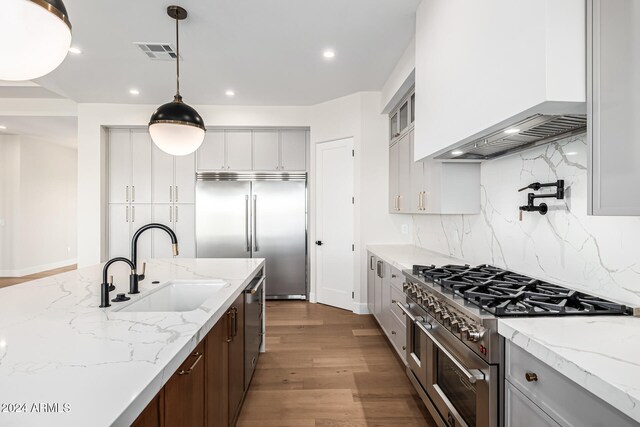 kitchen featuring premium appliances, light stone countertops, sink, dark hardwood / wood-style flooring, and pendant lighting