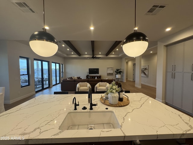 kitchen with a sink, light stone countertops, open floor plan, and visible vents
