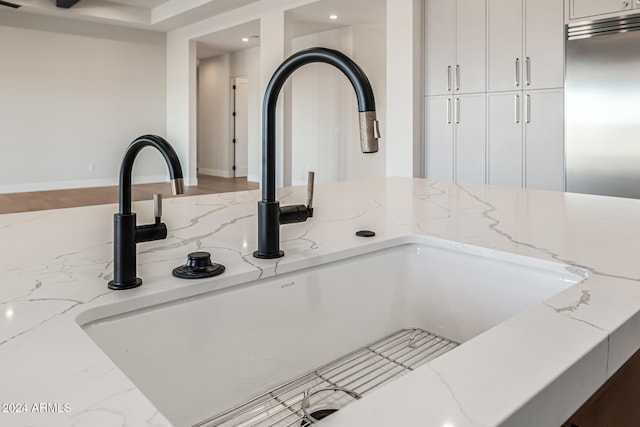 interior details with stainless steel built in fridge, white cabinetry, light stone countertops, and sink